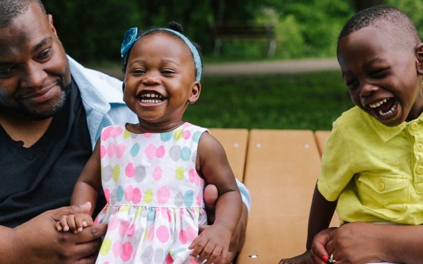 Black father with Black children one Black boy and one Black toddler girl laughing and smiling with a grass background